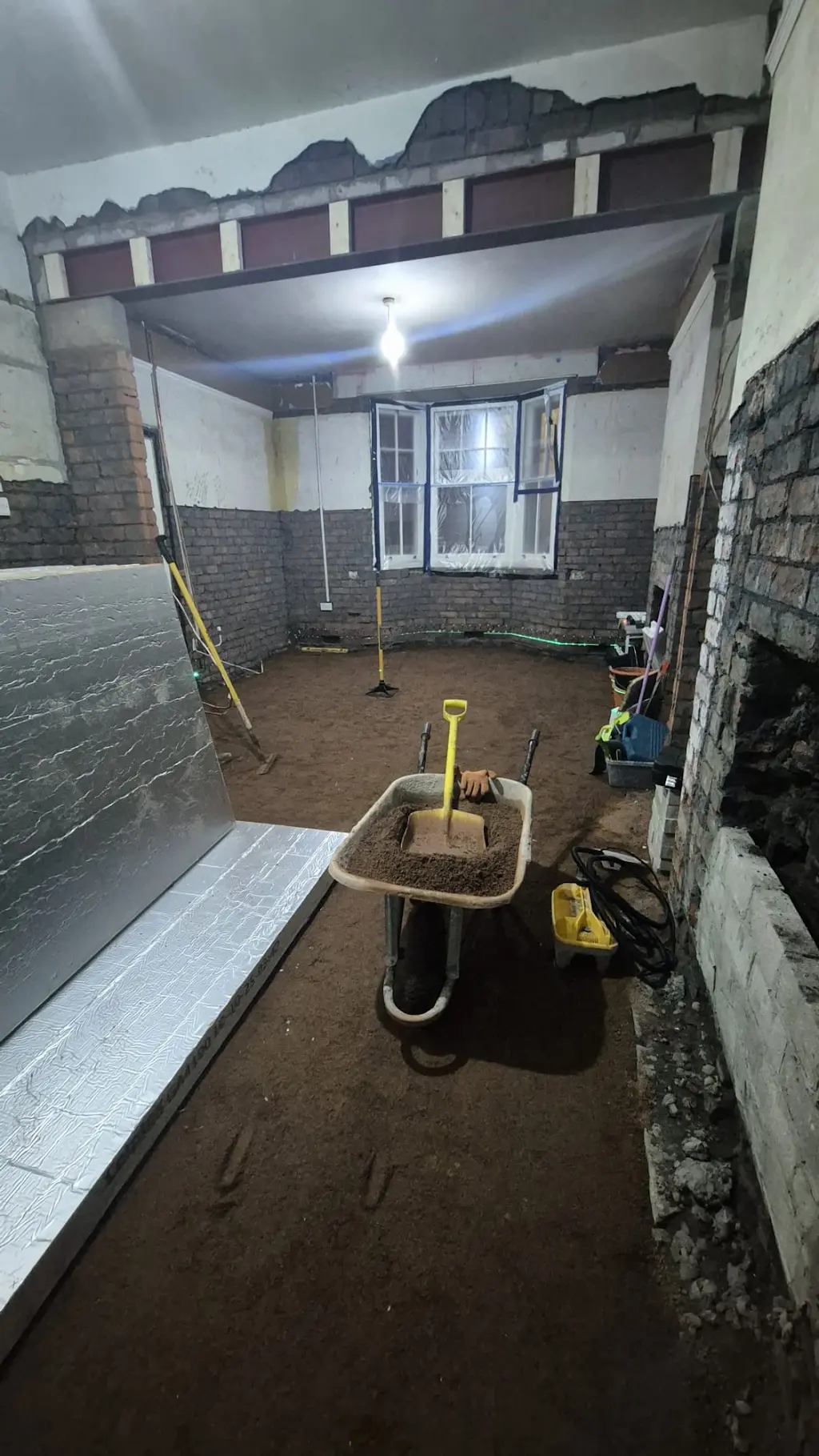 A wheelbarrow and levelling tools in the stripped room during floor preparation.
